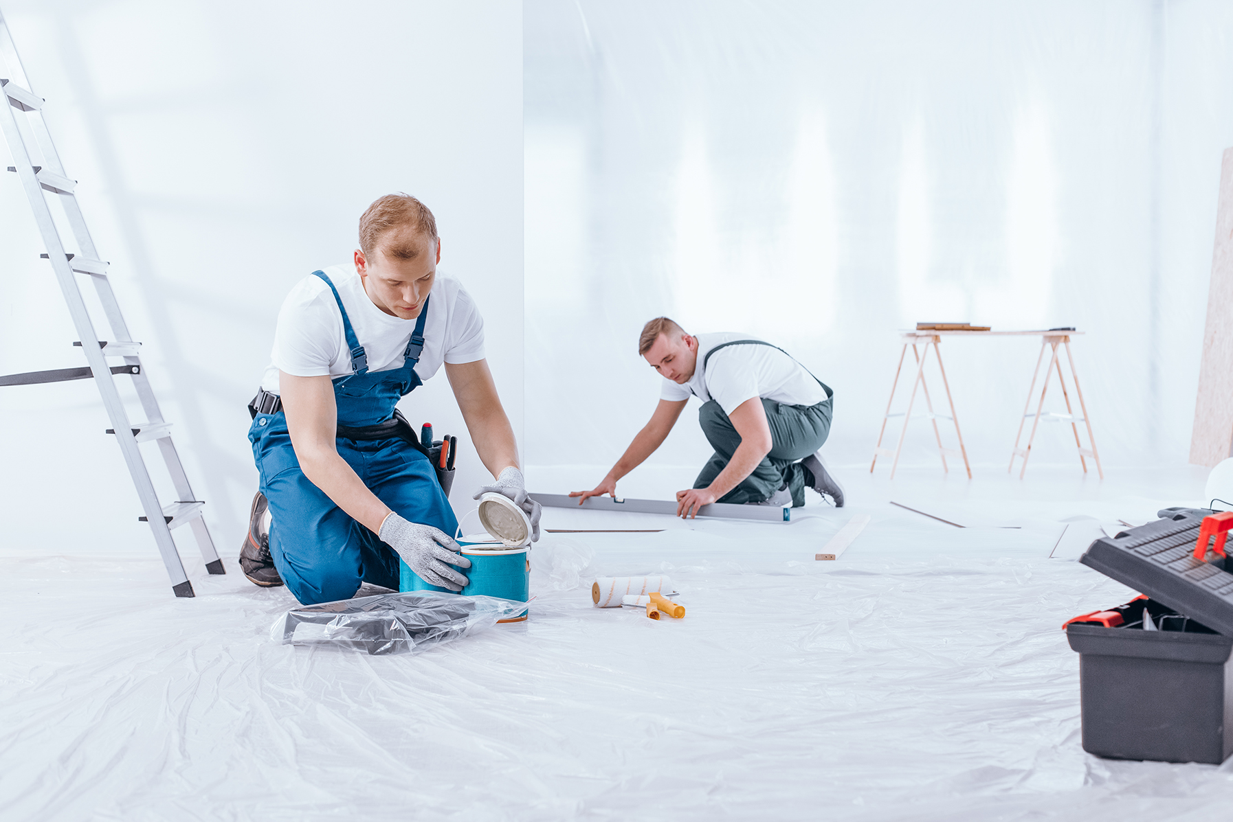 Professional architect in protective hardhat measuring wall with tape-line standing near step ladder construction safety and equipment during renovation process